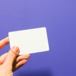 a hand holding a white business card against a purple background - AJ Bell ISA promotion offering a £100 Amazon Gift Card for new investors who deposit £10,000