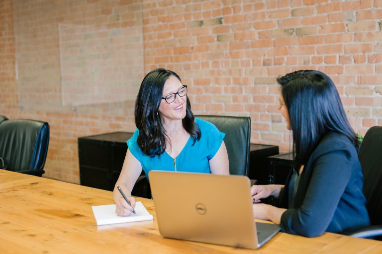 woman in teal t-shirt sitting beside woman in suit jacket - A retiree discussing retirement planning with a financial advisor, evaluating the pros and cons of professional financial advice