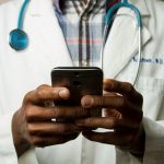 person wearing lavatory gown with green stethoscope on neck using phone while standing - A retiree reviewing healthcare costs and planning a budget for medical expenses in retirement