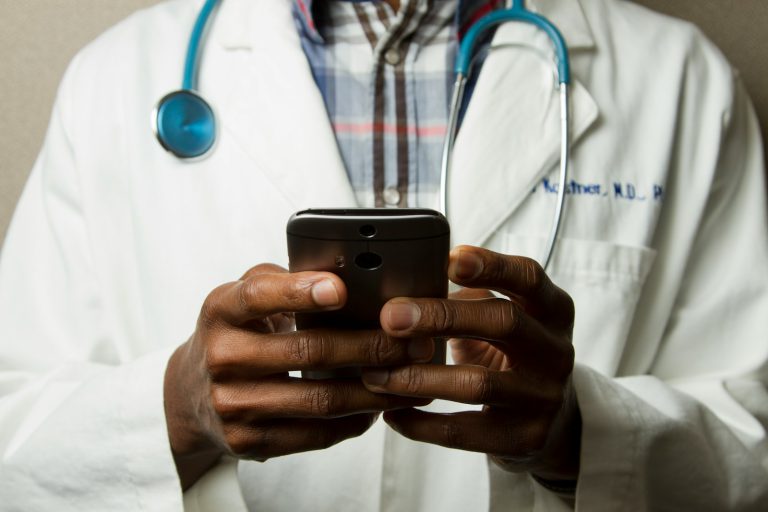 person wearing lavatory gown with green stethoscope on neck using phone while standing - A retiree reviewing healthcare costs and planning a budget for medical expenses in retirement