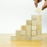 A person placing a piece of wood into a pyramid - A retiree reviewing ISA savings and investment options on a laptop