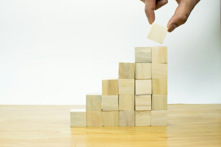 A person placing a piece of wood into a pyramid - A retiree reviewing ISA savings and investment options on a laptop