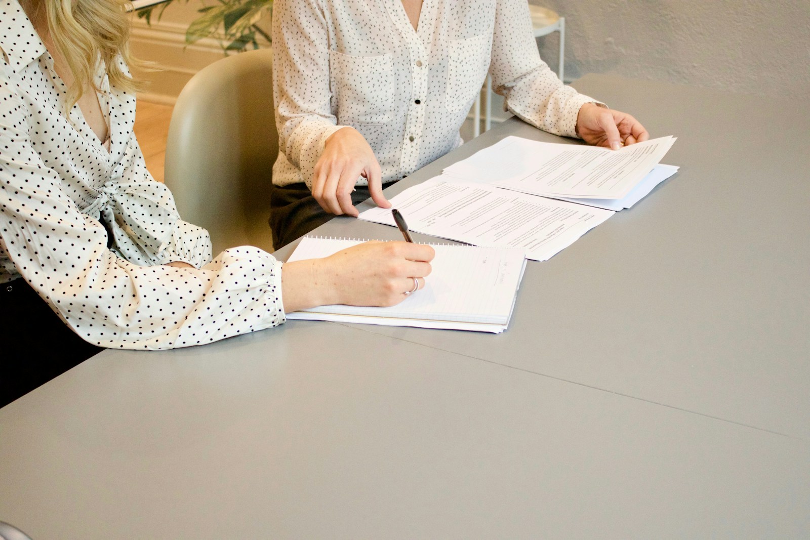 woman signing on white printer paper beside woman about to touch the documents - A retiree reviewing legal and administrative steps before retirement, ensuring all important documents and plans are in place