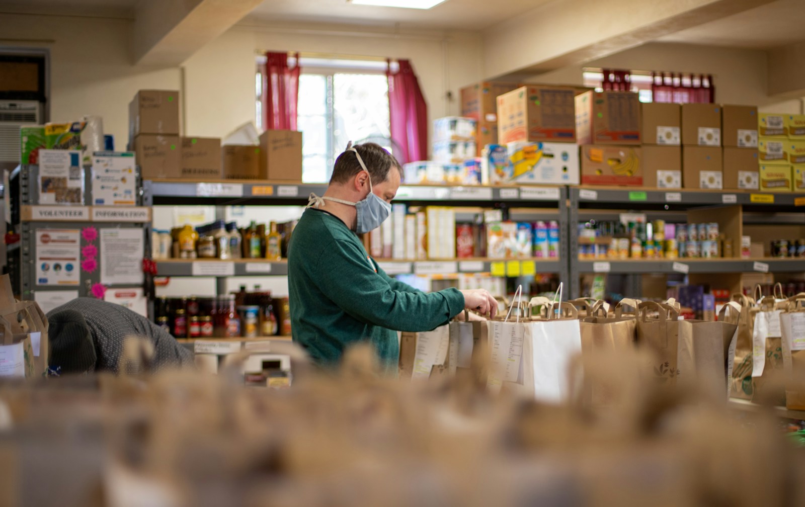 woman in green long sleeve shirt standing in front of clear glass jars - A retired volunteer helping in a charity shop, showing how retirees can give back to the community.